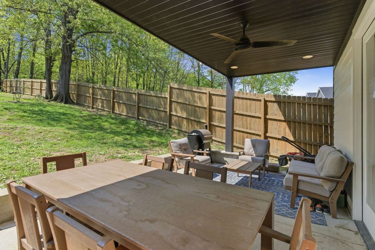 Backyard covered patio with tall privacy fence and view of open greenery.