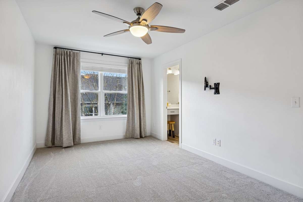 Spacious, light-filled primary bedroom featuring brand-new carpet throughout the entire upstairs level, a large window with custom blackout drapes, and access to a walk-in closet and en-suite bathroom.
