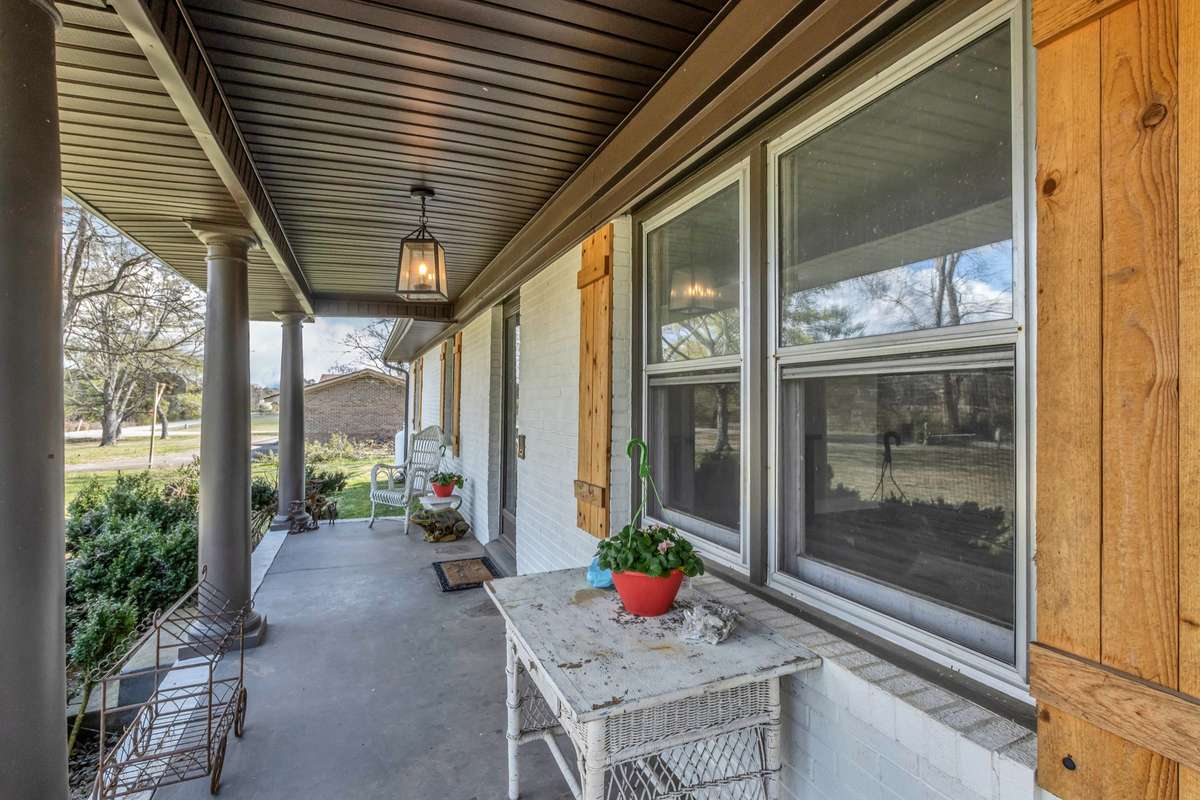 Rocking chair front porch overlooks farm across the road and big trees in front yard.
