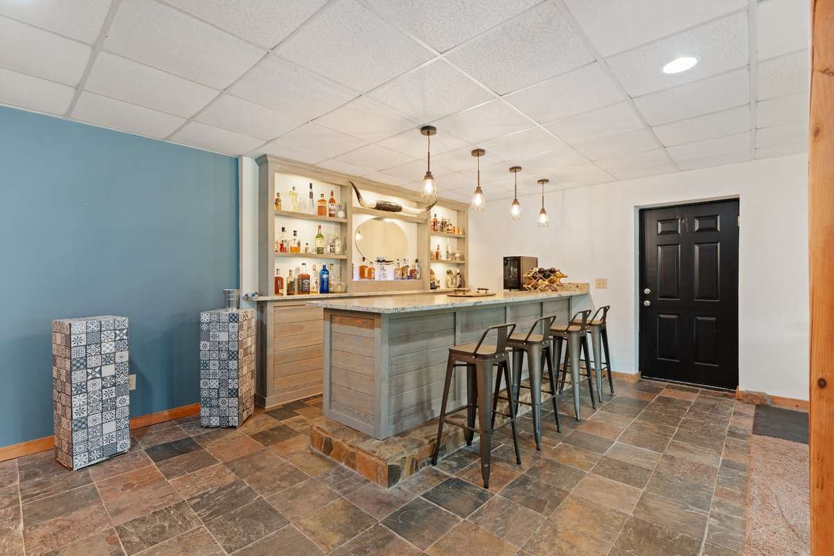 Basement custom built-in bar with back lit bottle shelving, storage and seating.