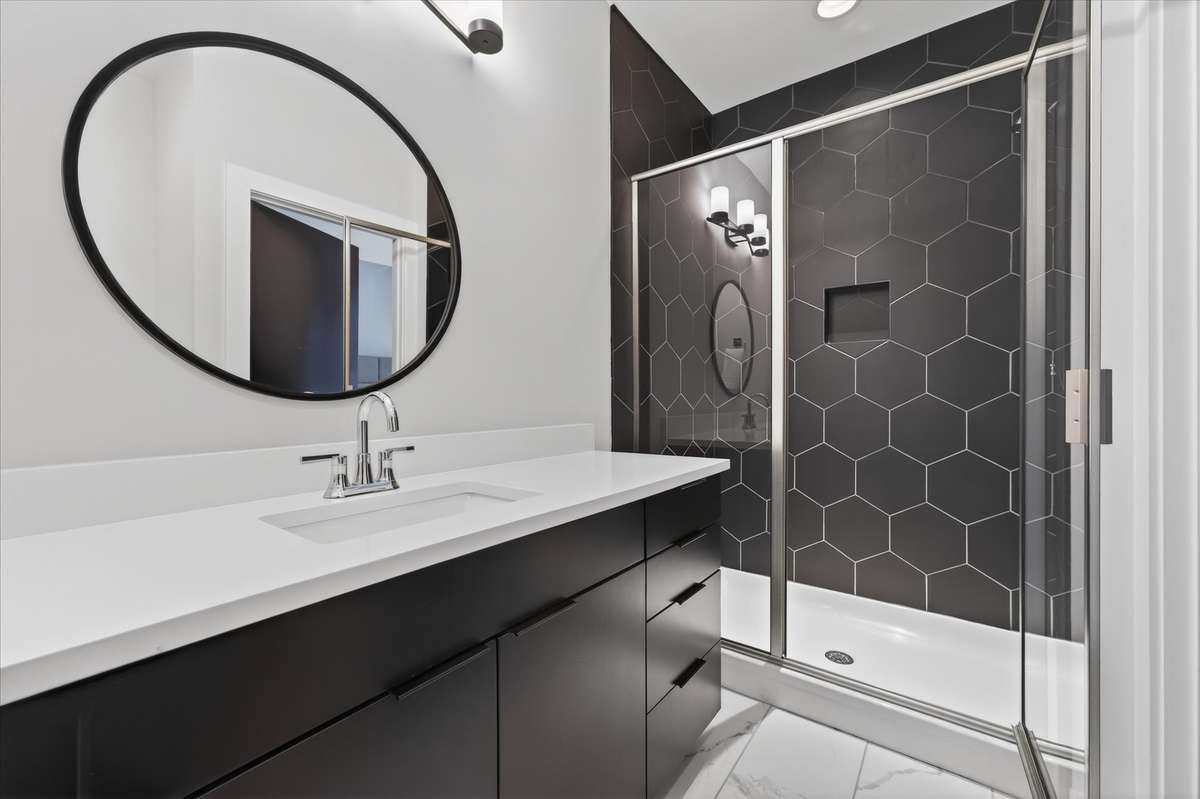 This luxurious ensuite bathroom features elegant marble tile floors, a spacious walk-in shower with striking black honeycomb hexagon walls, and a modern, sleek black-and-white design—a true retreat within this stylish suite.
