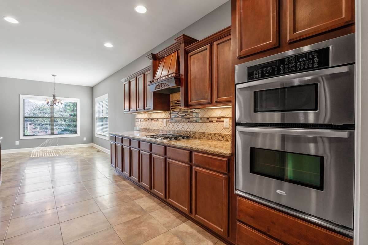 Gourmet kitchen with built-in gas oven, hood vent and gas cooktop, all stainless steel,  granite countertops, spacious cabinets, recessed lighting, and under-cabinet lighting—designed for effortless cooking, entertaining, and everyday living.