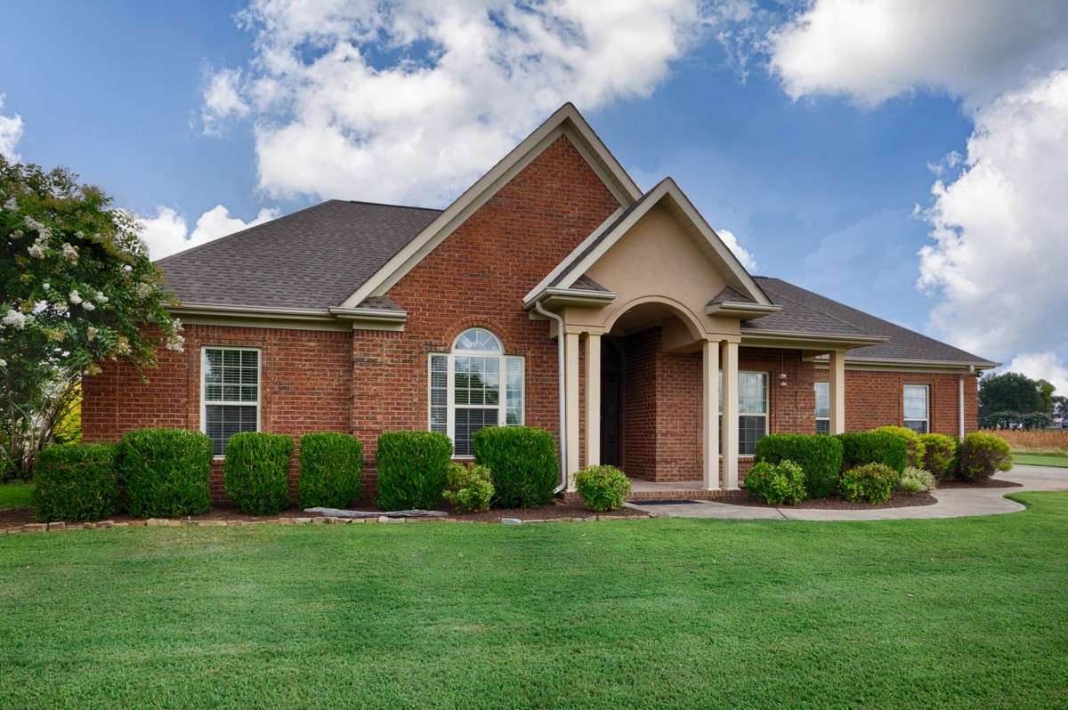 Front of house- Beautifully manicured lawn and landscaping, concrete driveway and sidewalk, full brick house, covered front porch with home entry