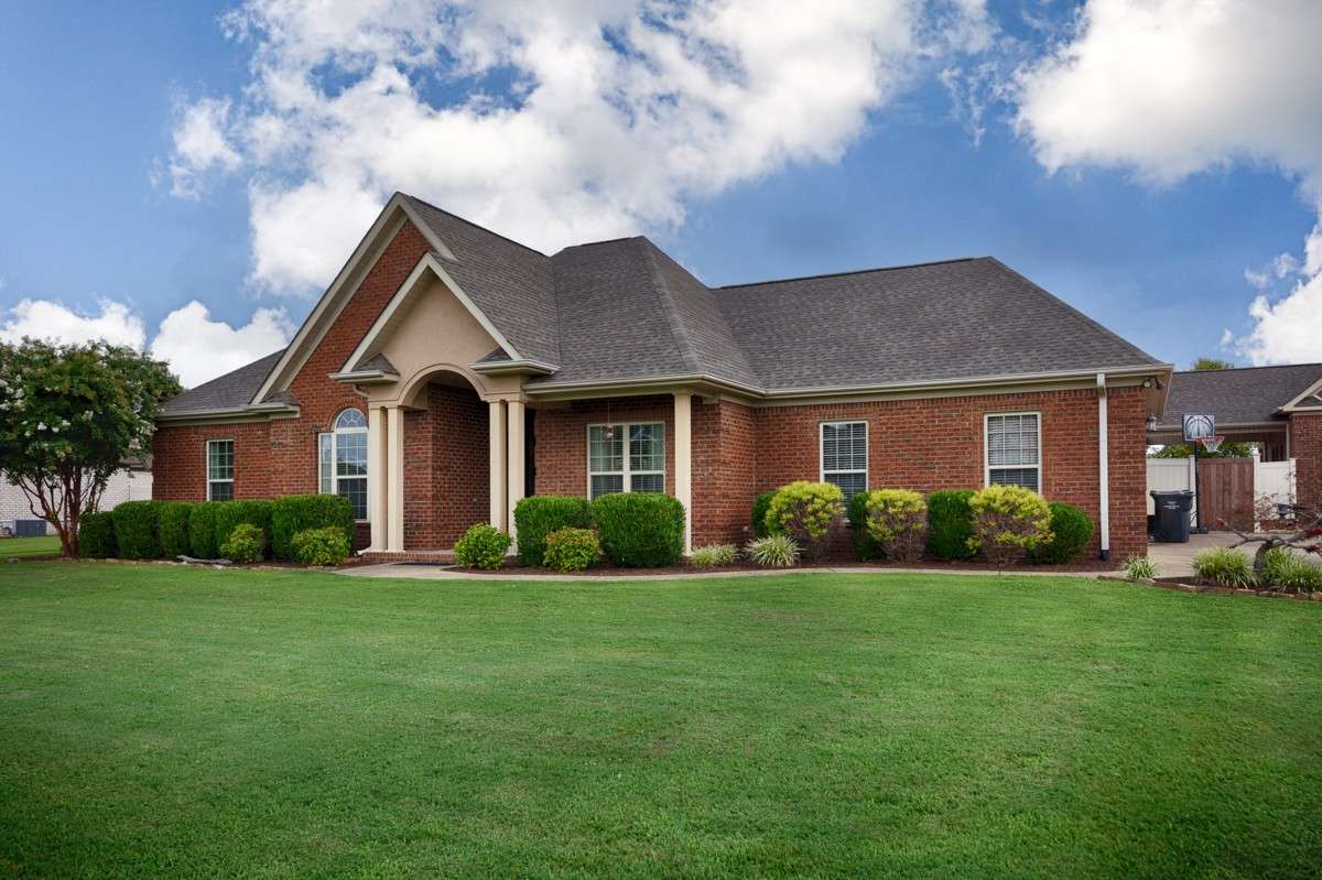 Front of house- Beautifully manicured lawn and landscaping, concrete driveway and sidewalk, full brick house, covered front porch with home entry