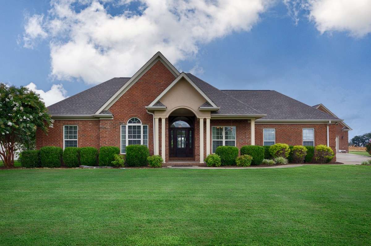 Front of house- Beautifully manicured lawn and landscaping, concrete driveway and sidewalk, full brick house, covered front porch with home entry