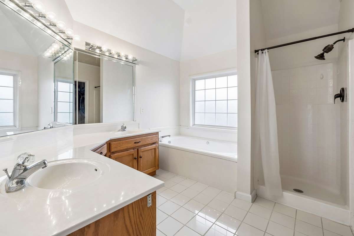 Primary bathroom featuring double vanities, a soaking tub beneath a large window, separate shower, and vaulted ceiling that adds extra light and openness to the space! 1407 Ottawa Place, Murfreesboro, TN 37129