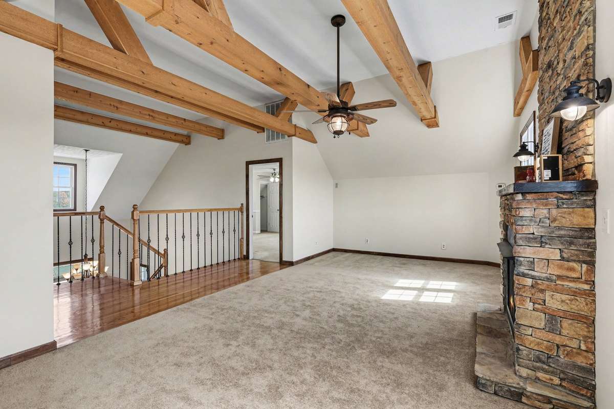 Another View of The Stunning Upstairs Den Featuring Exposed Wood Beams, A Cozy Stone Fireplace, And An Open View Overlooking The Grand Staircase Below
