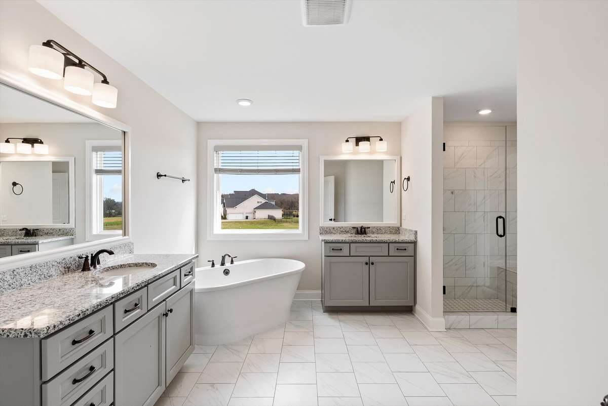 Primary bathroom featuring dual vanities, a soaking tub with views, and a separate glass-enclosed shower—designed for both comfort and functionality.