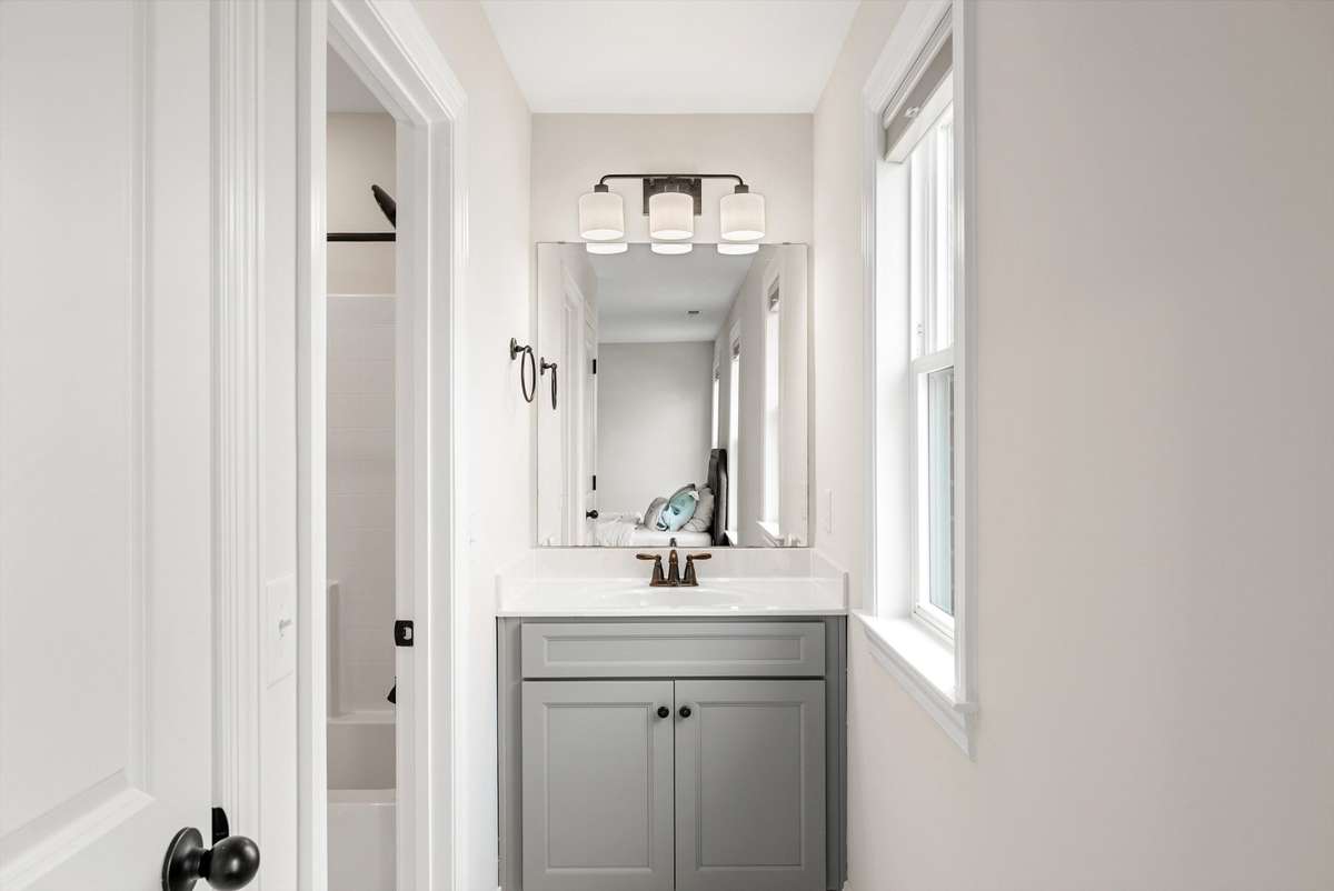 Bright and efficient vanity area with modern lighting and natural light, thoughtfully positioned between adjoining spaces for everyday functionality.