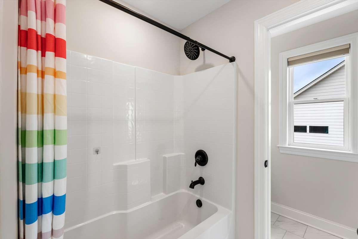 Bright and cheerful bathroom with a tub/shower combo, clean finishes, and natural light from the nearby window.
