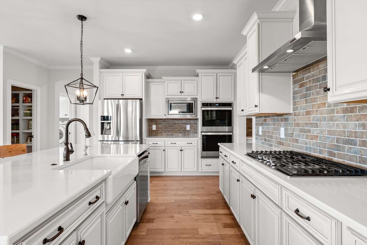 Bright, timeless kitchen featuring crisp white cabinetry, apron sink, quartz countertops, stainless steel appliances, and a spacious island designed for both everyday living and effortless entertaining.