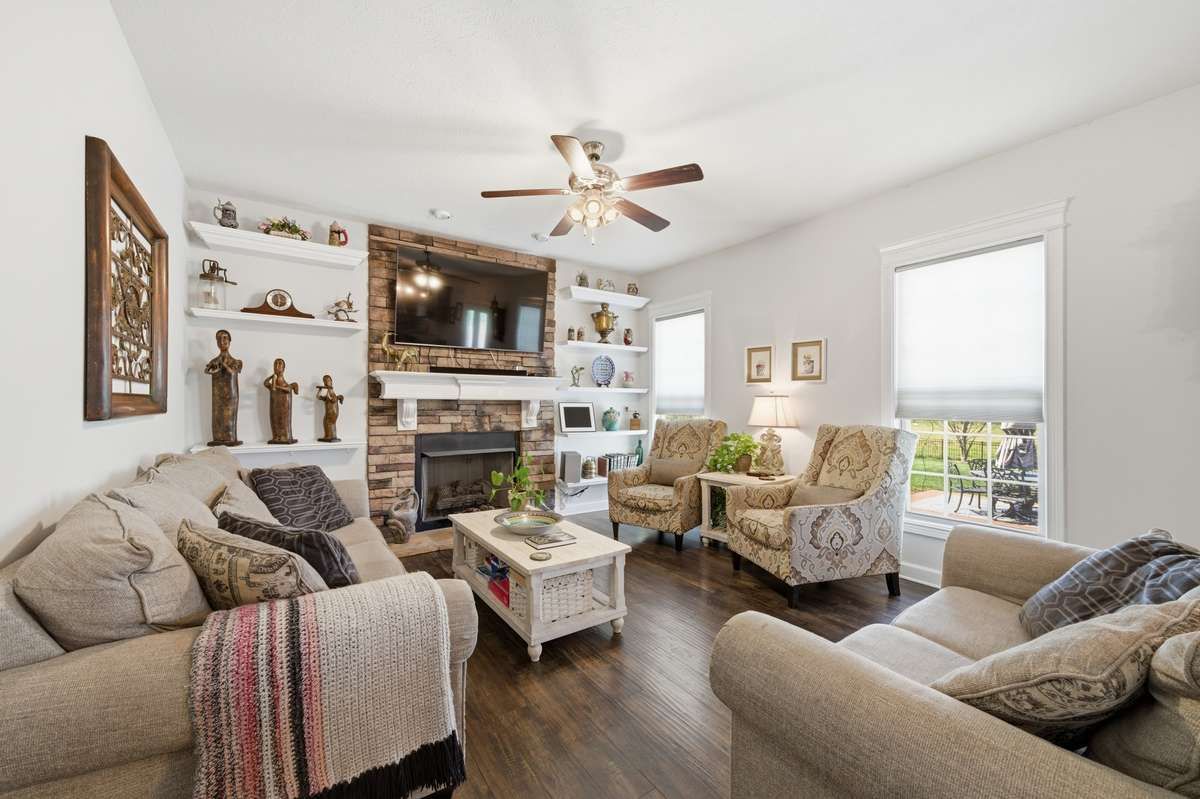 Inviting living room featuring a stone fireplace, custom built-ins, hardwood floors, and abundant natural light.