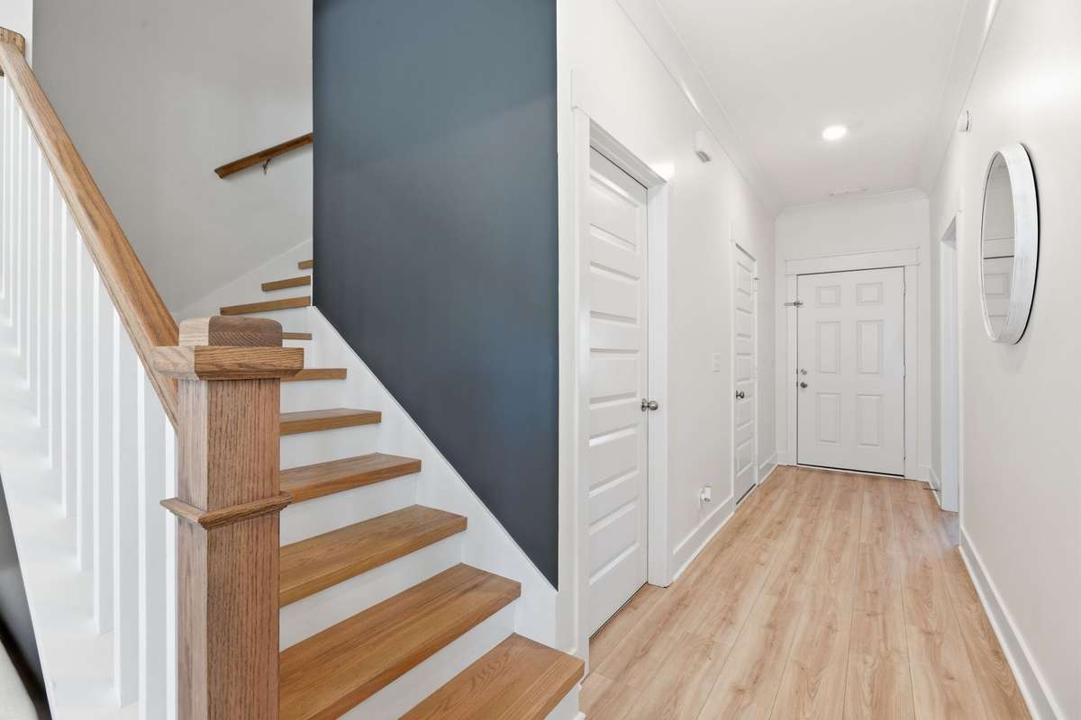 The staircase showcases laminate flooring with crisp white accents and a stylish accent wall, adding a modern touch. The accent wall beneath the stairs features a space designed for your beloved pet to have their own little room.