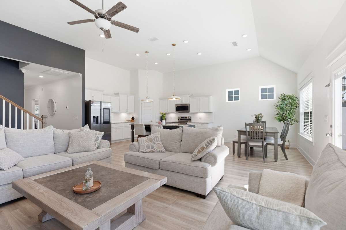 Bright and airy open-concept living space featuring soaring vaulted ceilings, abundant natural light, and a seamless flow between the living, dining, and kitchen areas. The spacious living room is anchored by neutral tones and modern finishes.