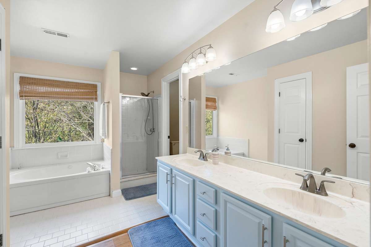The primary suite bathroom features a double sink vanity, tile & laminate flooring, jetted tub, and stand up shower.