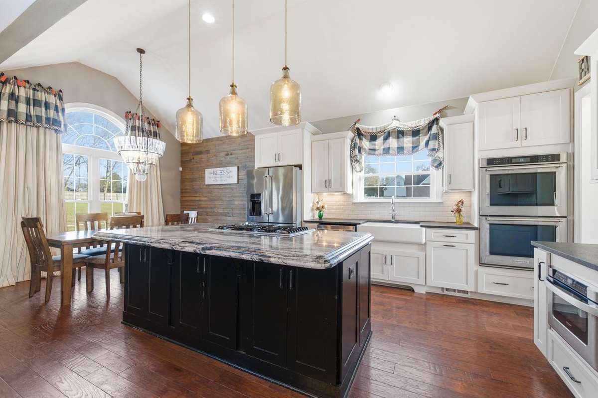 The kitchen features a large island with a spacious eat-in area, a farmhouse sink, soaring ceilings, and custom lighting, creating a bright and inviting space perfect for gathering.