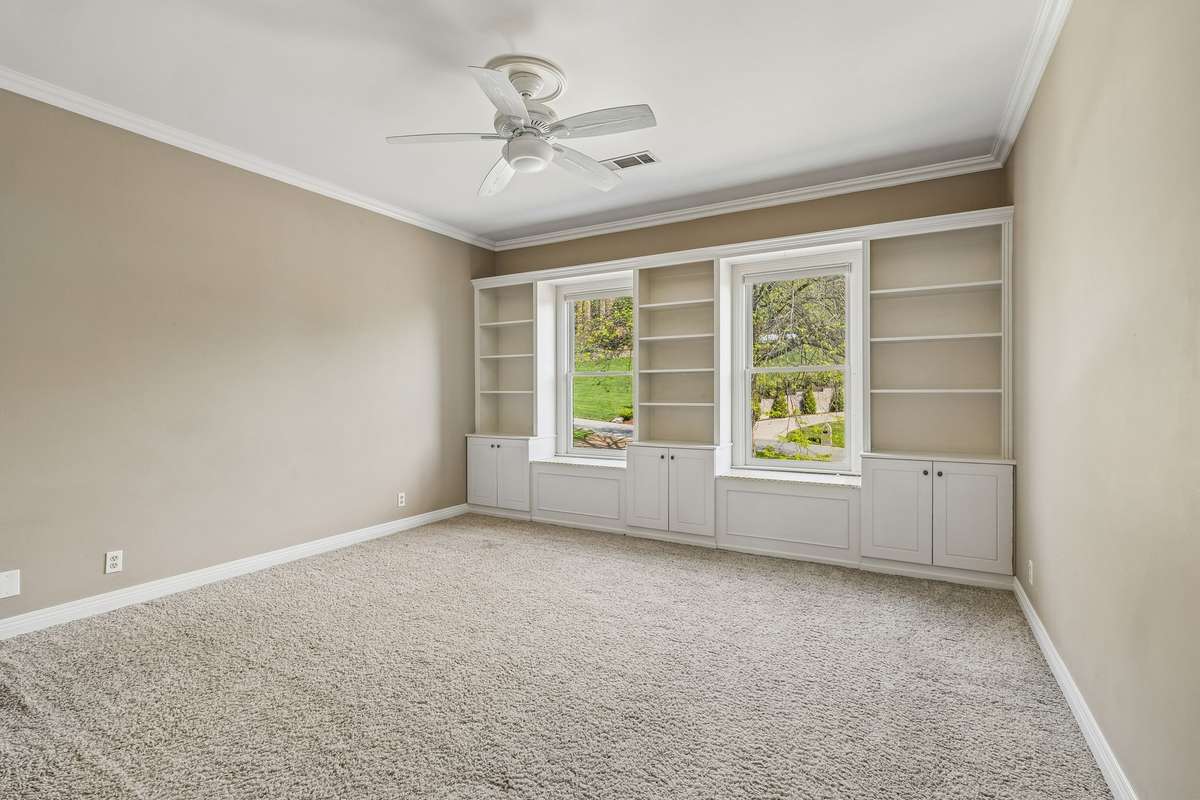 One of the front bedrooms offers sunny views overlooking lush landscaping outdoors and features convenient cabinetry and shelving.
