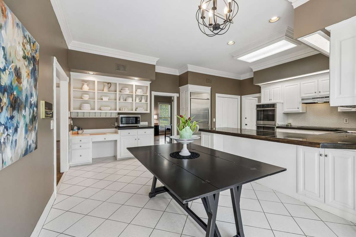 The kitchen is the central hub of the home and currently offers a desk area with open shelving above, white cabinetry, and walkout access to the picturesque back yard setting.