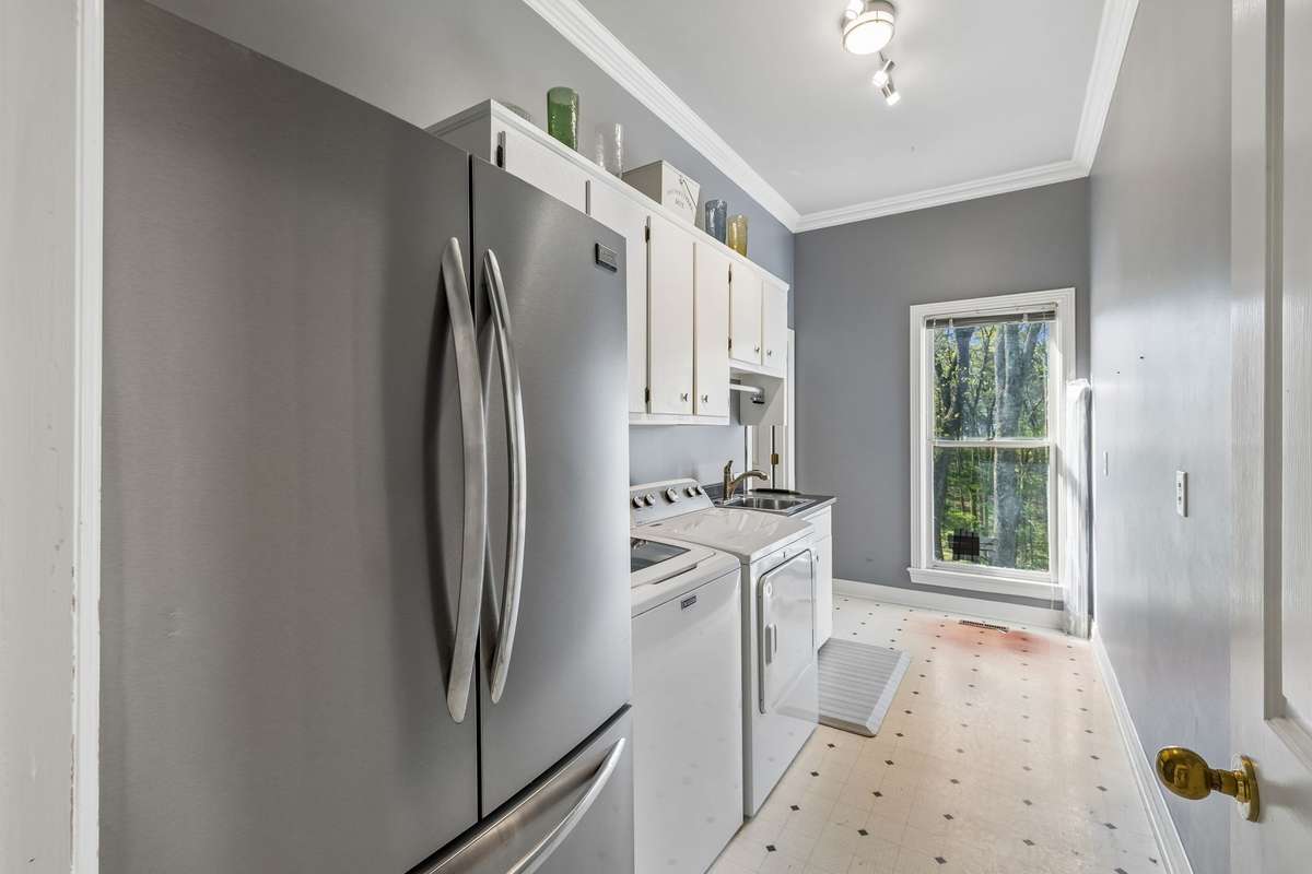 The main level laundry room contains a stainless refrigerator that remains with the home.  To the left of the window (which is being replaced) is a oversized additional pantry, perfect for housing appliances and extra food supplies.