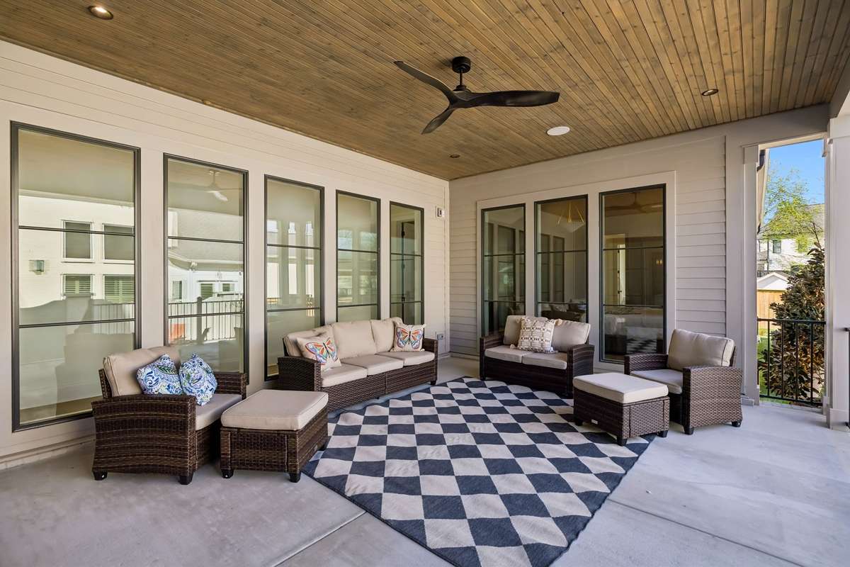 Covered outdoor living space designed for year-round enjoyment, featuring a warm wood ceiling, ceiling fan, and ample room for comfortable seating and entertaining. Seamlessly connected to the interior through multiple windows and doors.