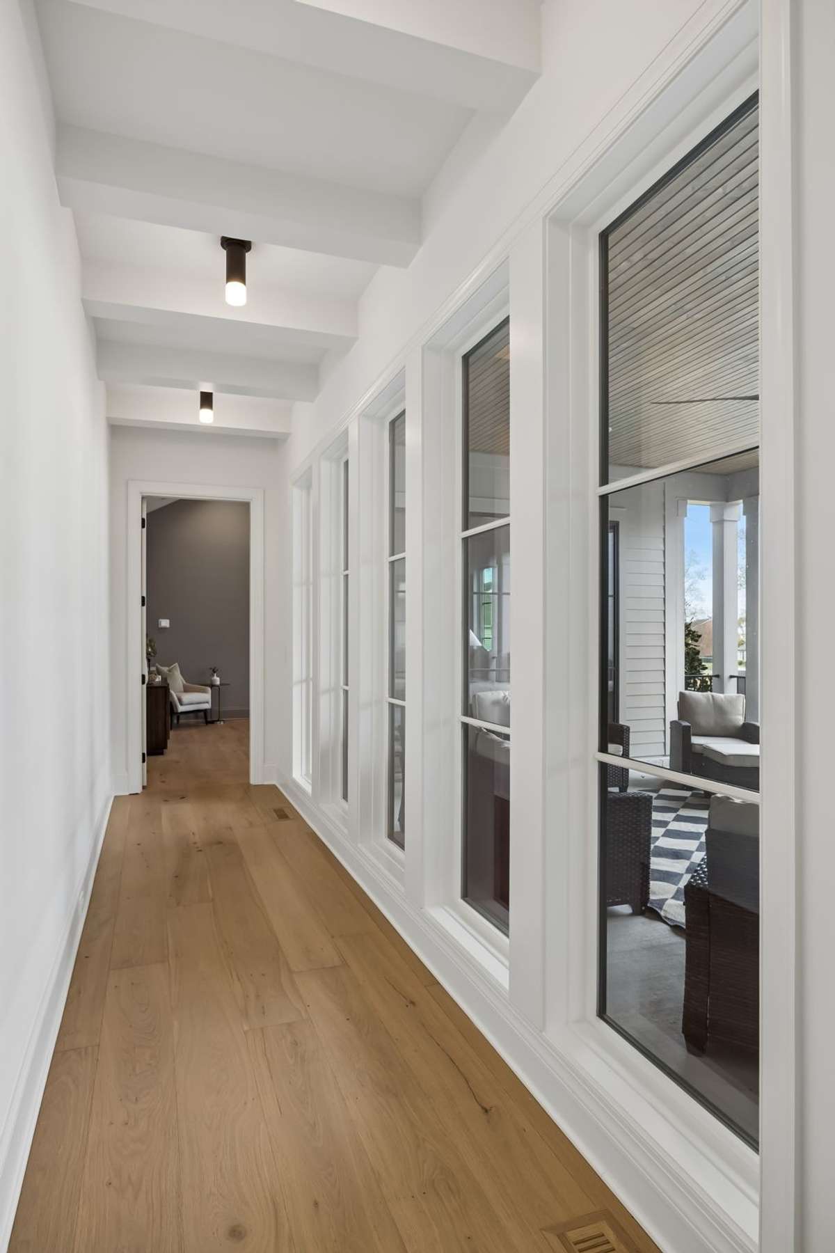 A stunning gallery-style hallway lined with oversized windows creates a light-filled transition from the main living area to the private primary suite. This thoughtfully designed passage brings in natural light while offering views of the covered out