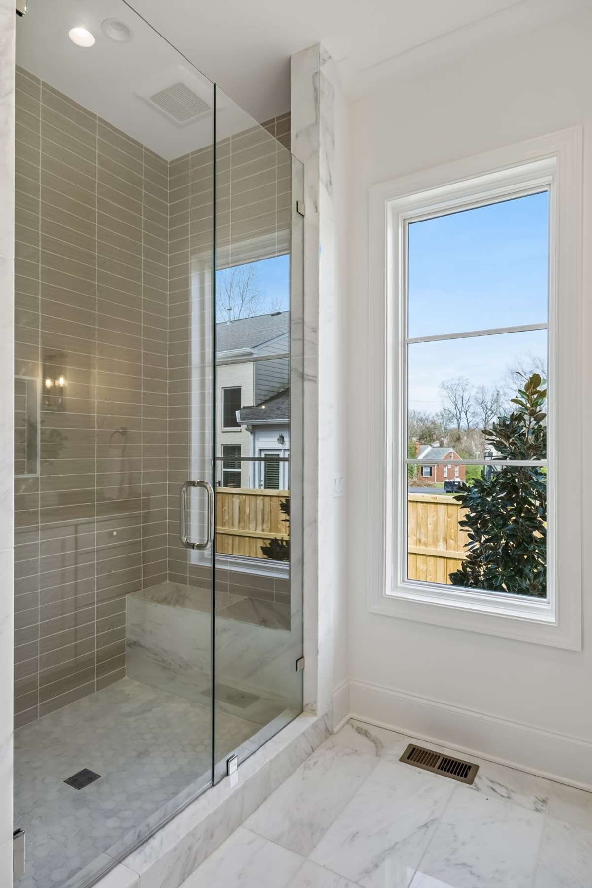Spa-inspired bath featuring a marble-topped vanity with custom cabinetry and elegant lighting. The glass-enclosed walk-in shower is finished with designer tile and natural light, creating a bright, clean, and luxurious retreat.
