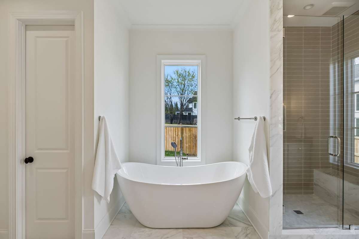 Spa-inspired bath featuring a marble-topped vanity with custom cabinetry and elegant lighting. The glass-enclosed walk-in shower is finished with designer tile and natural light, creating a bright, clean, and luxurious retreat.