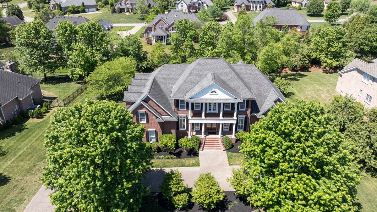 This stately all-brick home features shade trees and a manicured lawn, with elegant steps and a balcony overlooking the circular driveway