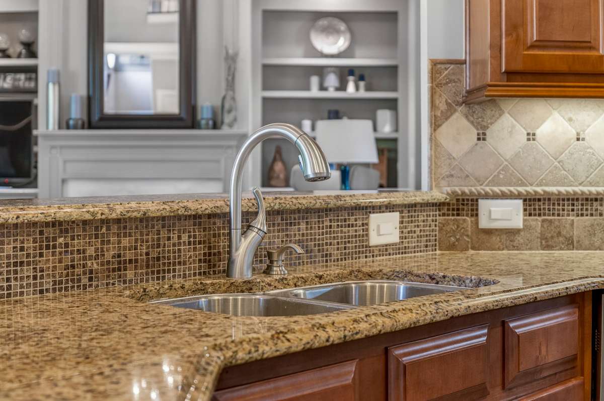 A close up of the granite countertops and backsplash grants us an inviting view of the living room, making multitasking easy.