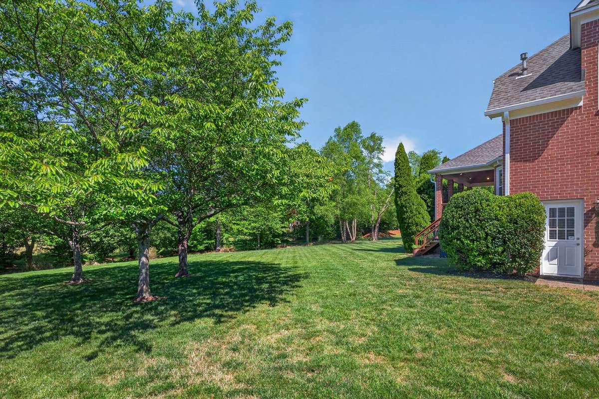 The deck steps descend to a green backyard and level lot, with plenty of shade trees and well-maintained landscaping.
