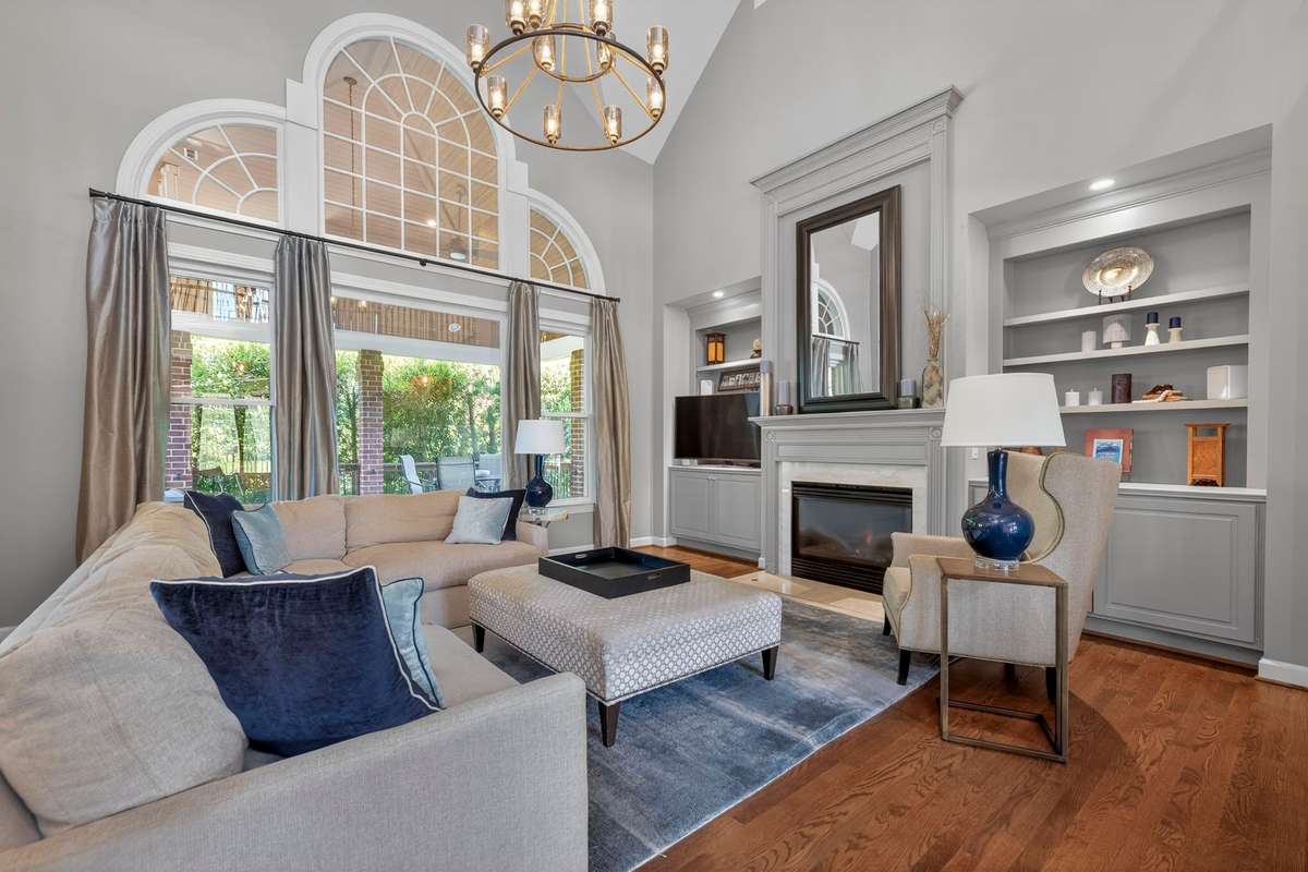 Light-filled living room with soaring ceilings, dramatic arched windows, gas fireplace, designer lighting, and custom built-ins flanking a cozy fireplace—perfectly blending elegance and comfort.