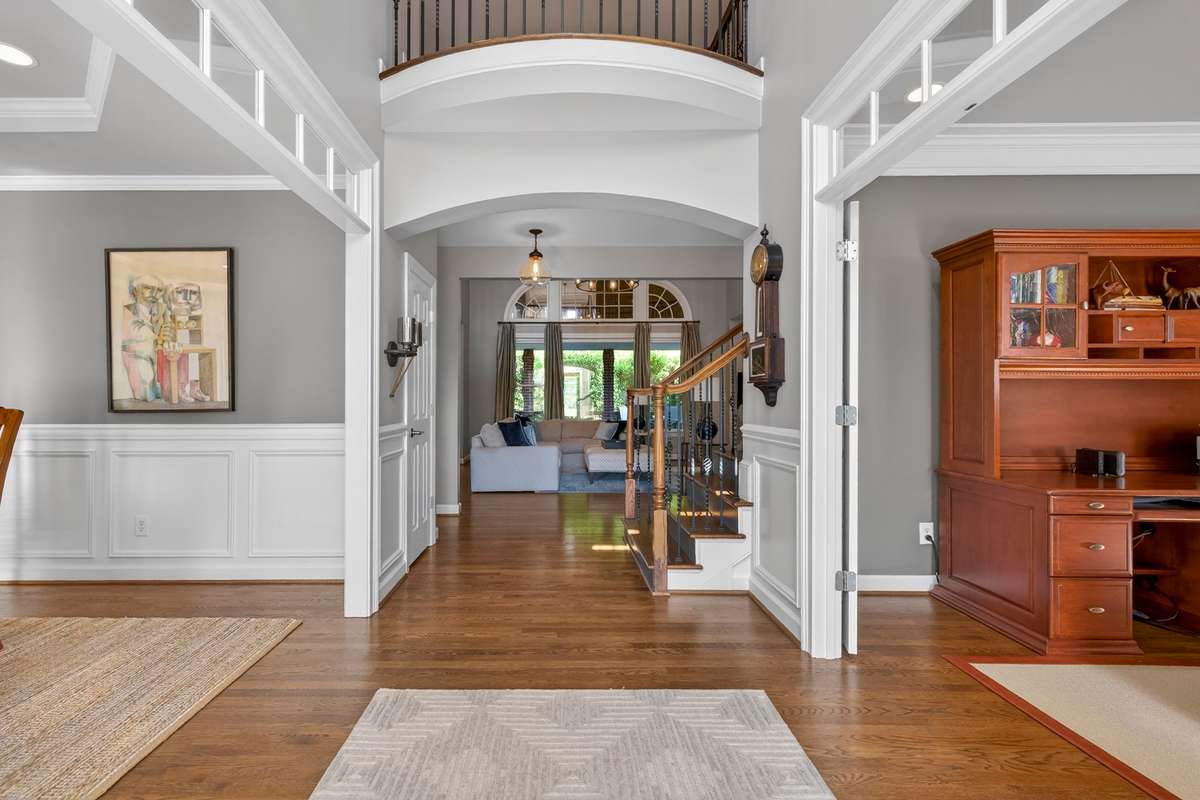 A welcoming foyer features archways and curved balcony railings overhead. To the right lies the home office with an elegant set of French doors, and to the left, the spacious dining room.