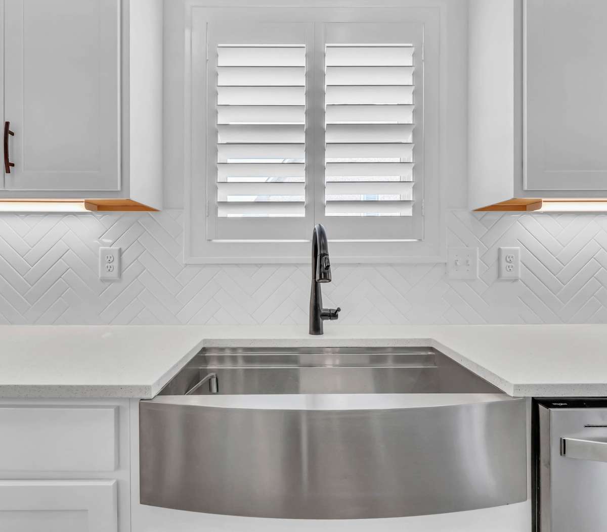 The classic herringbone tile backsplash adds subtle texture and elegance, while the window above—complete with plantation shutters—fills the space with natural light.  The stainless sink is a bonus!