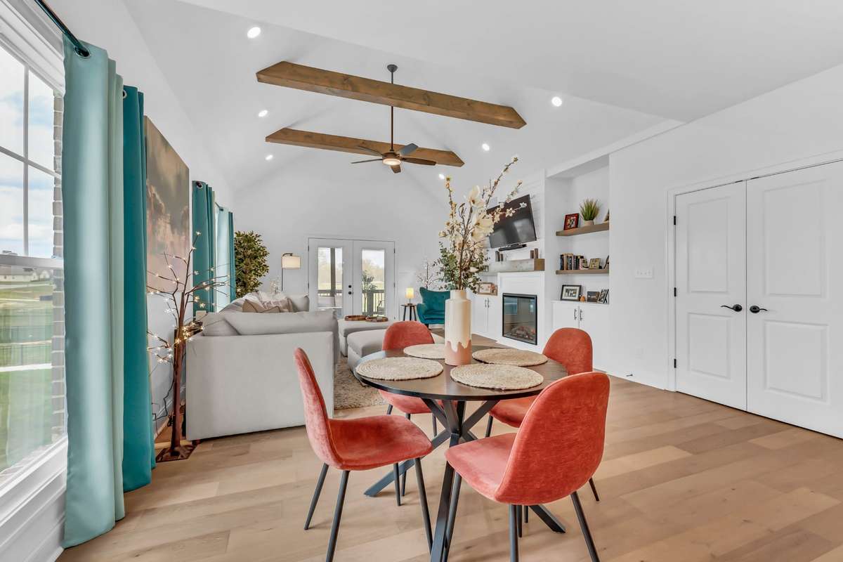 Vaulted ceilings with exposed wood beams create a stunning architectural focal point, while large windows and glass doors fill the space with natural light. The cozy living area features a modern fireplace with built-in shelving, adding charm.