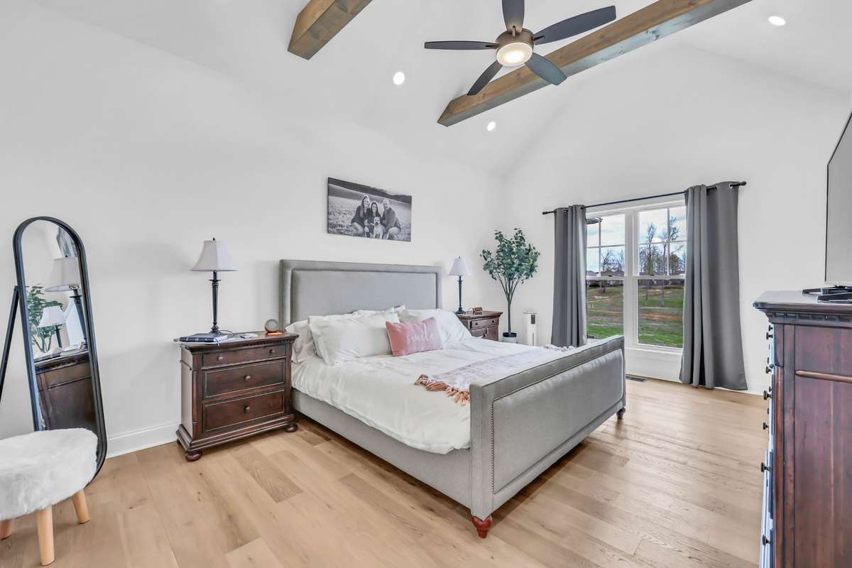 This spacious primary bedroom offers a peaceful retreat with a perfect blend of comfort, neutral tones, and style. Vaulted ceilings with exposed wood beams create an open, airy feel, while large windows bring in an abundance of natural light.