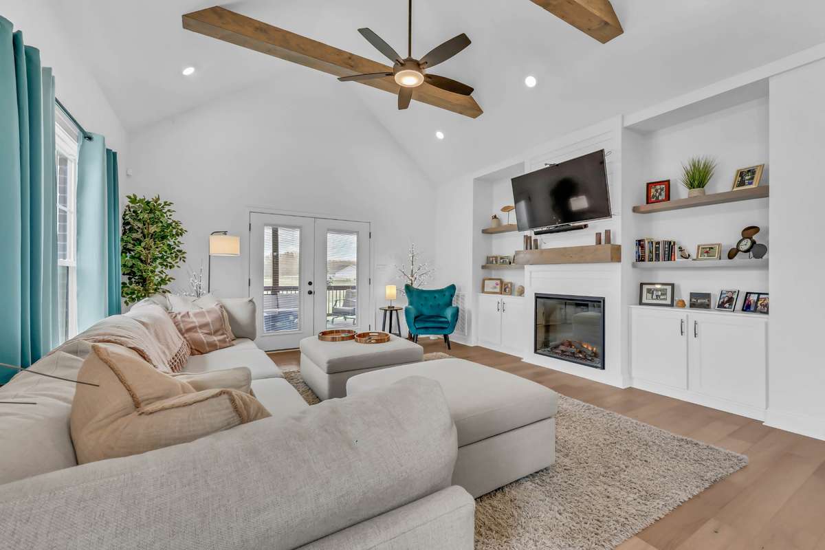 Vaulted ceilings with exposed wood beams create a striking architectural feature, while recessed lighting, built-in shelving, and a ceiling fan add both function and ambiance.