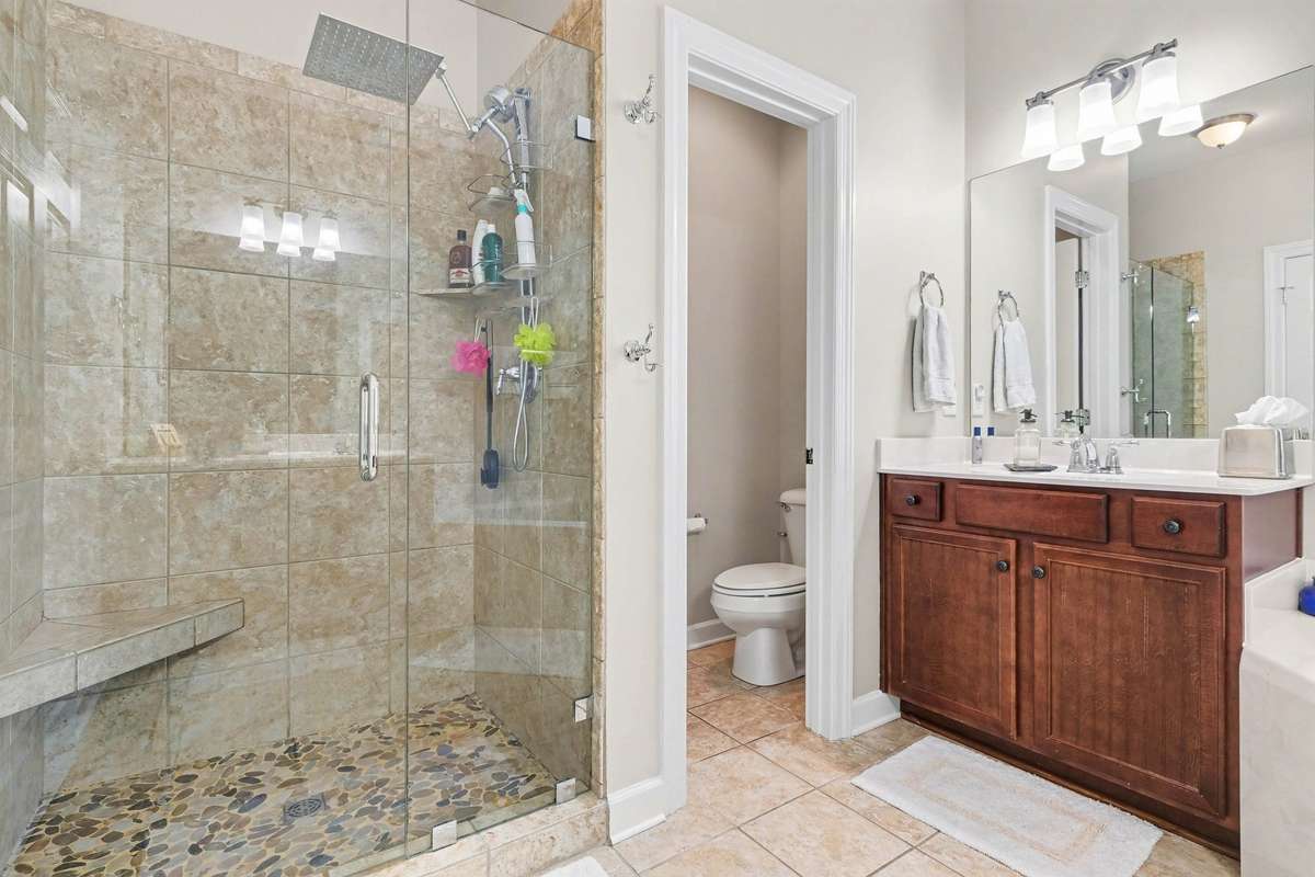 Spa-like primary en suite featuring a large walk-in glass shower with tile surround, bench seating, and upgraded fixtures.