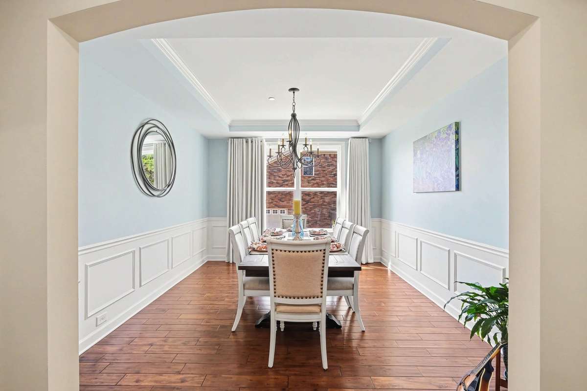 Framed by an elegant archway, this formal dining room makes a striking first impression with its tray ceiling, detailed wainscoting, and rich hardwood floors.