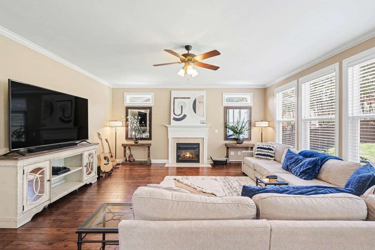 Comfortable, light-filled living room centered around a cozy fireplace, with large windows with plenty of natural light, stylish finishes, and space to relax or entertain.