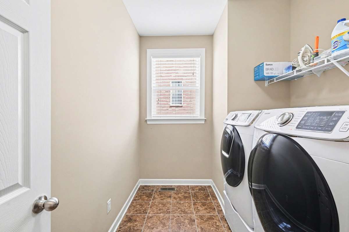 Functional and efficient laundry room featuring full-size washer and dryer, durable tile flooring, and a convenient utility shelf for storage.