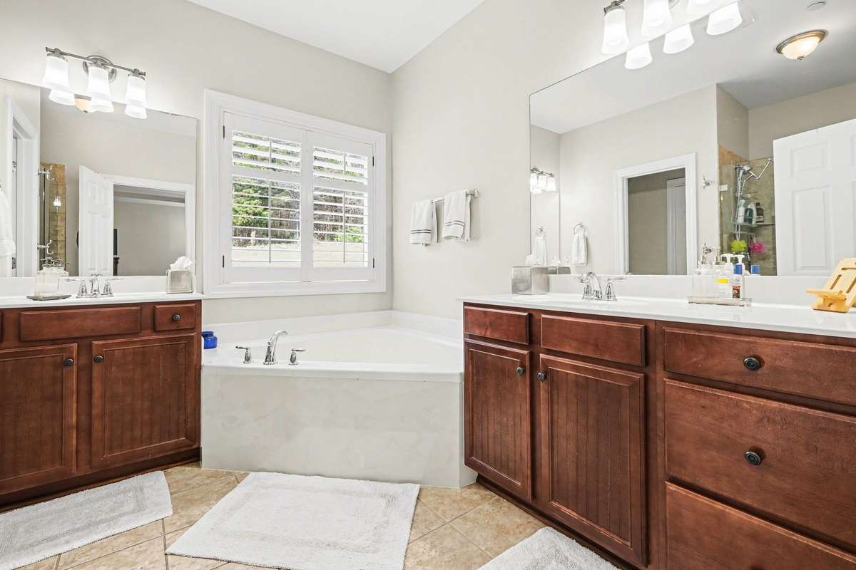 Bright and spacious primary en suite featuring dual vanities with ample storage, a soaking tub framed by a large window, and elegant finishes throughout.