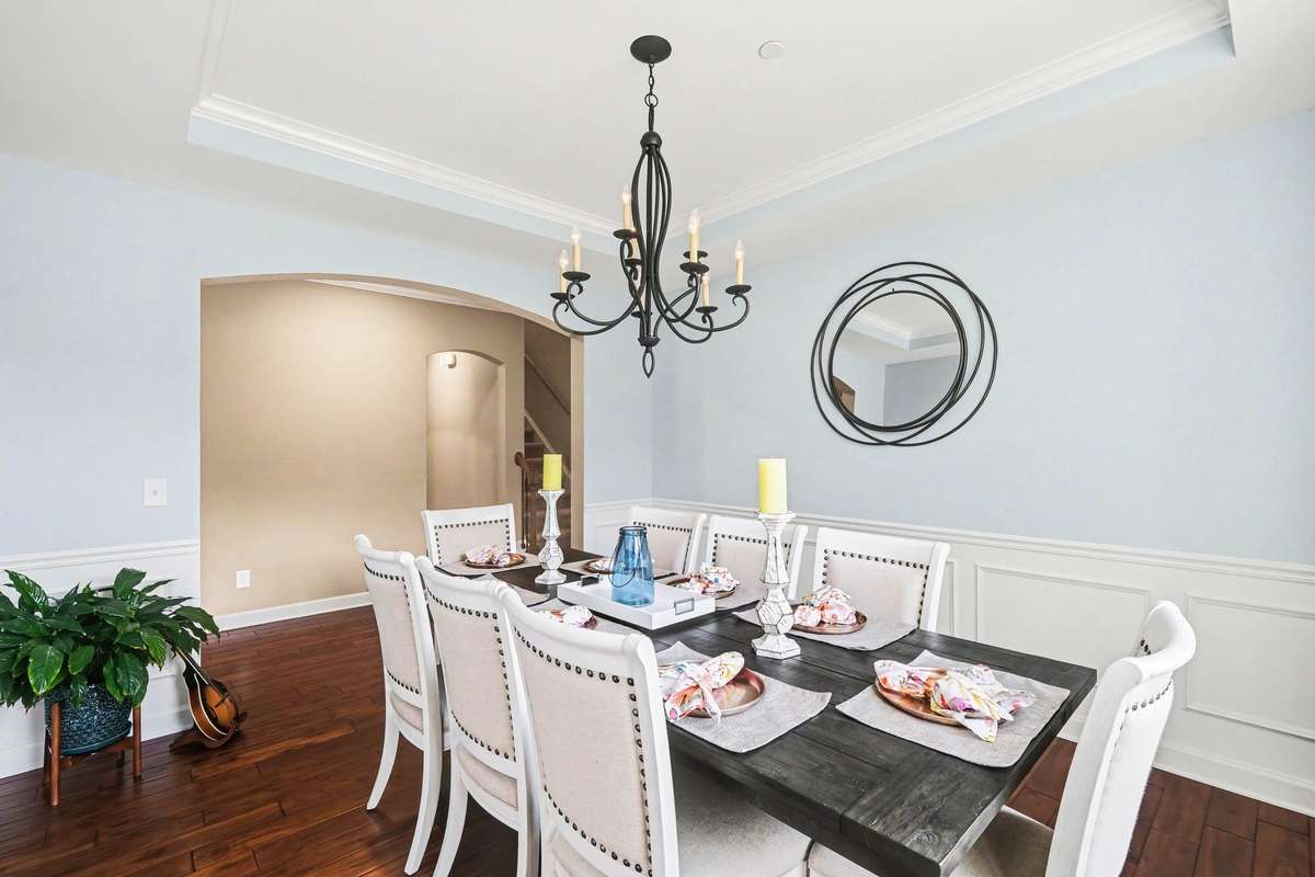 Elegant formal dining room with rich hardwood floors, classic wainscoting, and a tray ceiling. A stylish chandelier and spacious layout make it perfect for entertaining, with an open flow to adjacent living areas.