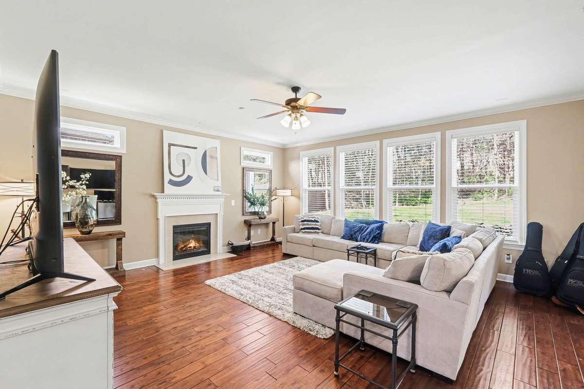 Spacious, sun-filled living room with gleaming hardwood floors, a cozy fireplace, and expansive windows