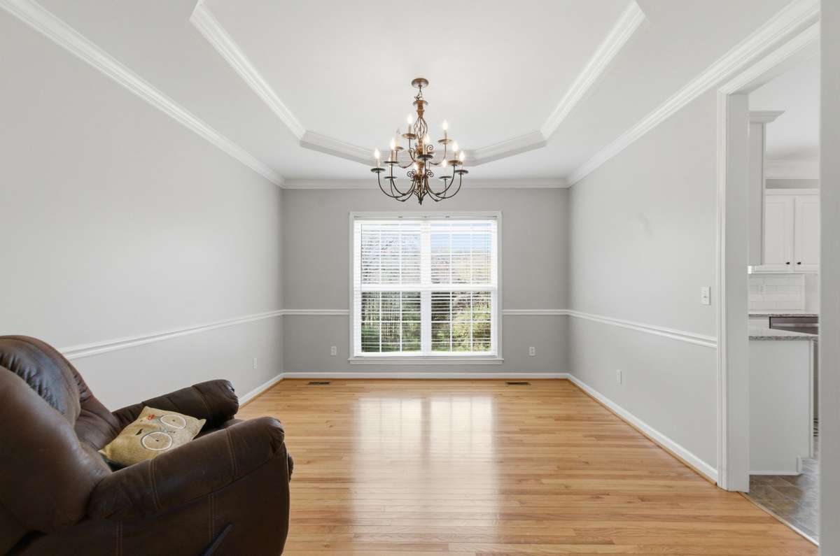 Elegant dining space with tray ceiling, crown molding, and a statement chandelier, complemented by large windows for natural light.