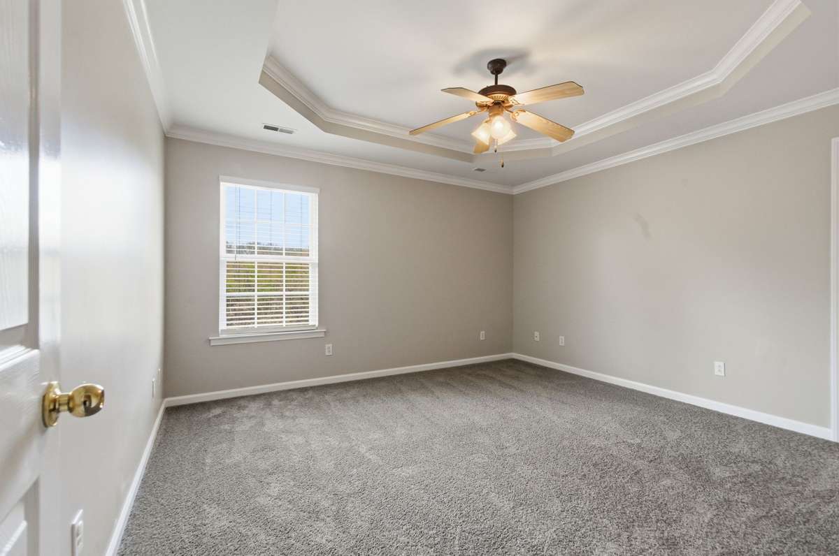 Spacious bedroom featuring a tray ceiling with crown molding, plush carpeting, and a large window for natural light.