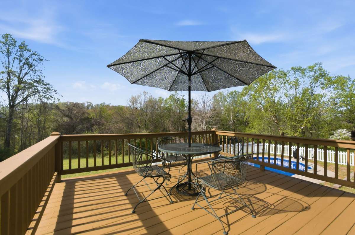 Elevated deck with space for seating and dining, overlooking a spacious backyard with mature trees—ideal for relaxing or entertaining.