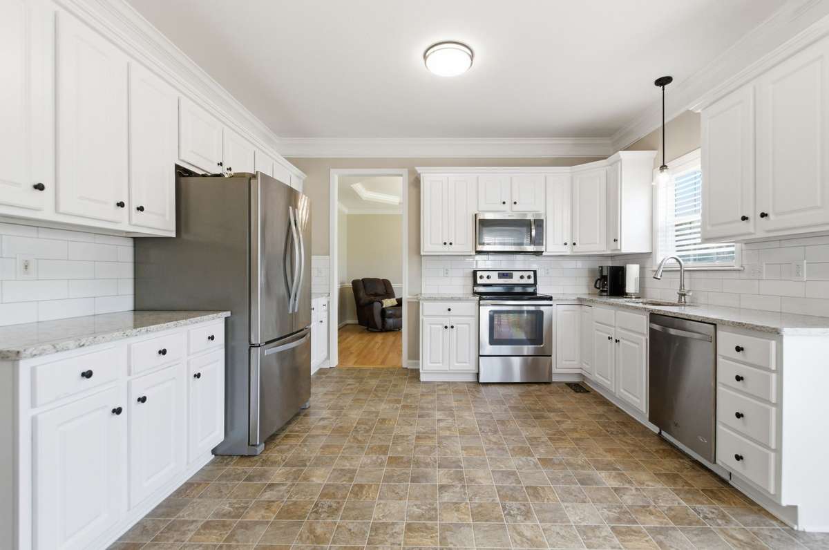 Well-appointed kitchen featuring granite countertops, stainless steel appliances, white cabinetry, and a clean tile backsplash.