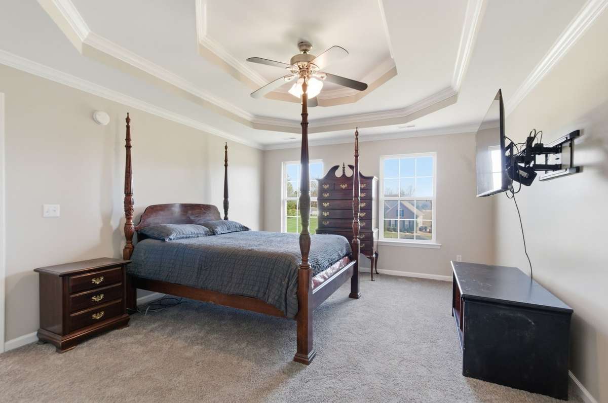 Generously sized primary suite with tray ceiling, crown molding, and multiple windows providing abundant natural light.