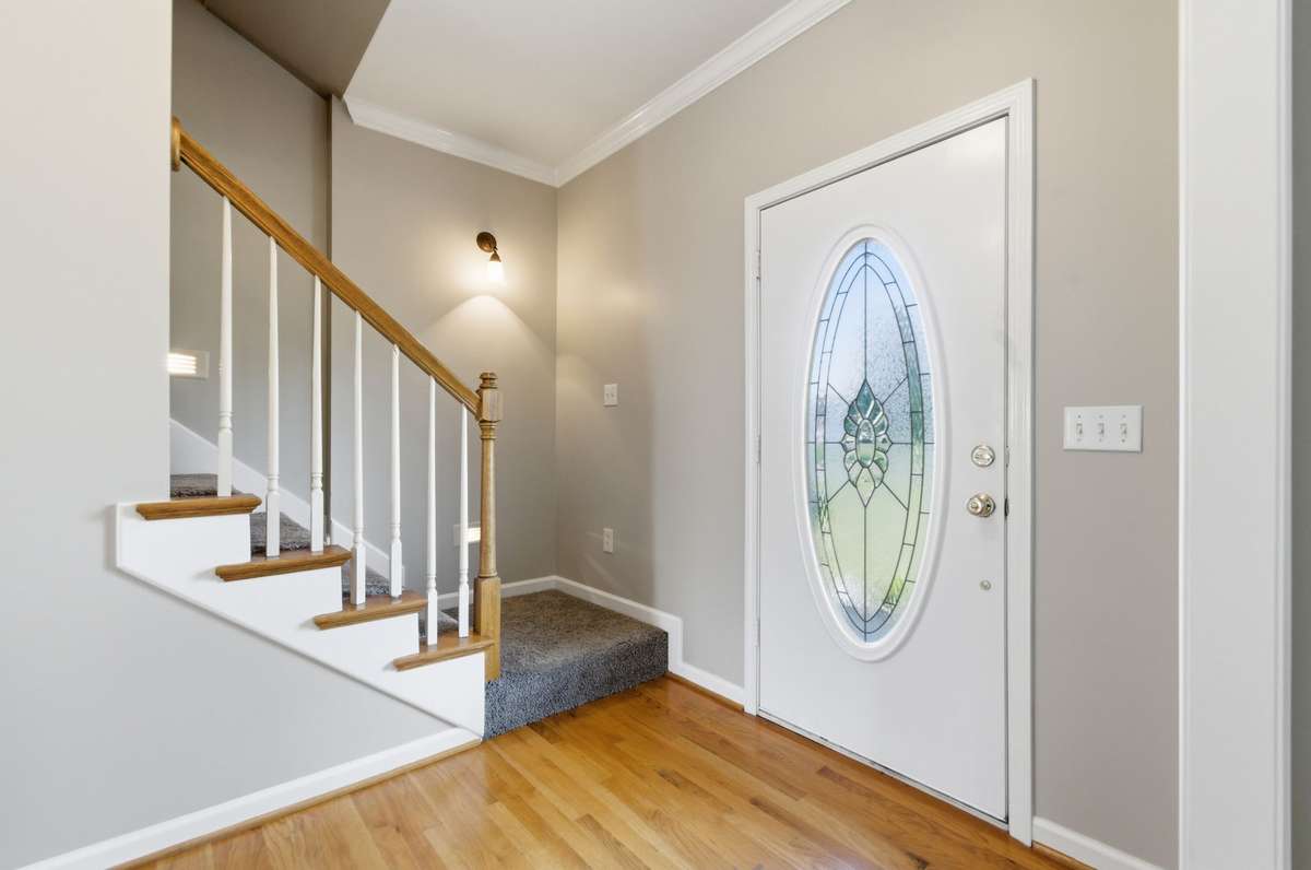 Bright entryway with hardwood flooring, crown molding, and a staircase featuring wood accents and classic railing details.