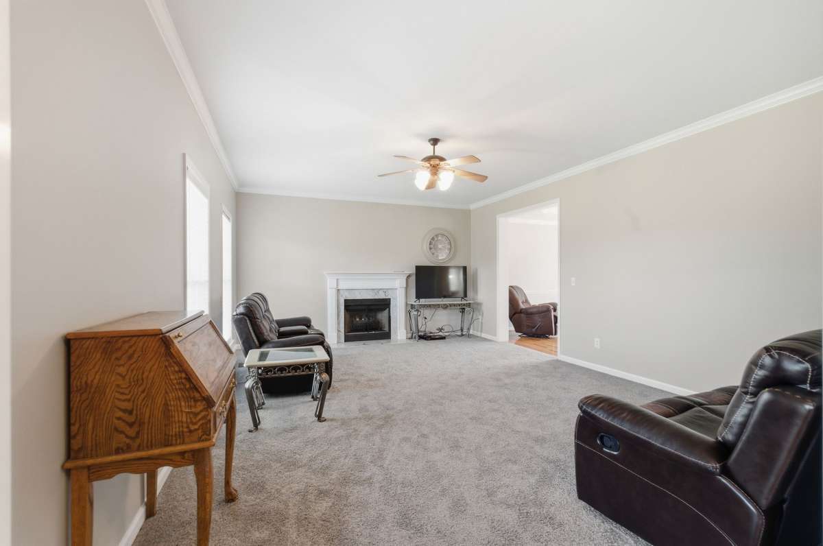Spacious living room with plush carpeting, a central fireplace with mantel, and abundant natural light from multiple windows.
